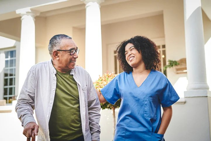 senior man and his female caregiver smile while on a scenic walk outside of Claridge Court Senior Living Community