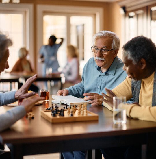 group of senior friends discuss chess moves during a game at their senior living community