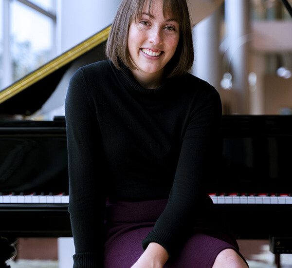 25 year old music student Beth Christensen sits in front of a grand piano at Claridge Court Senior Living Community, smiling