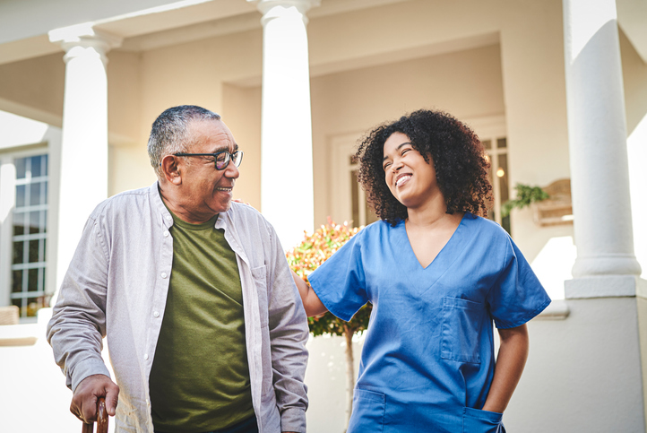 senior man and his female caregiver smile while on a scenic walk outside of Claridge Court Senior Living Community