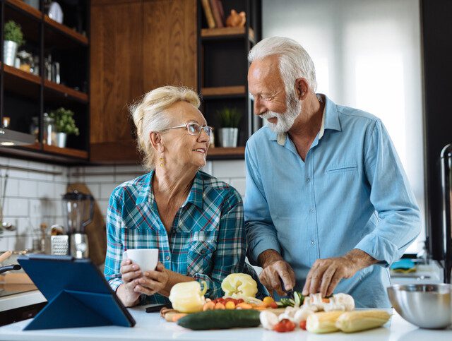 senior couple looks lovingly at one another while preparing a meal in their kitchen