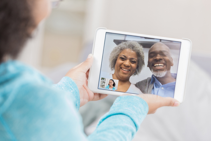 young granddaughter holds tablet, video calling her smiling grandparents