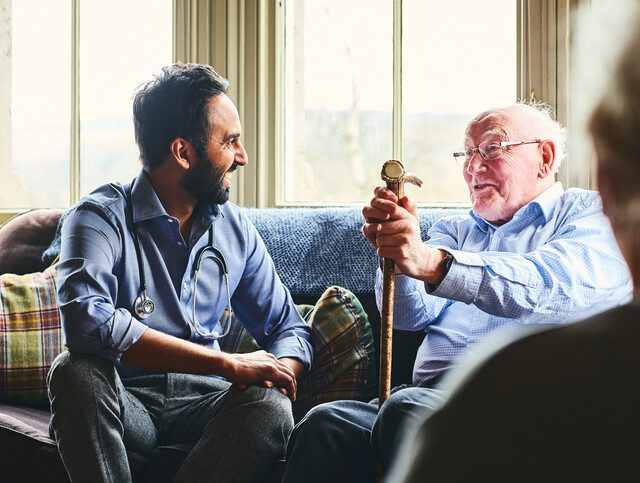 seated senior man with cane smiles and talks with his adult son, seated next to him