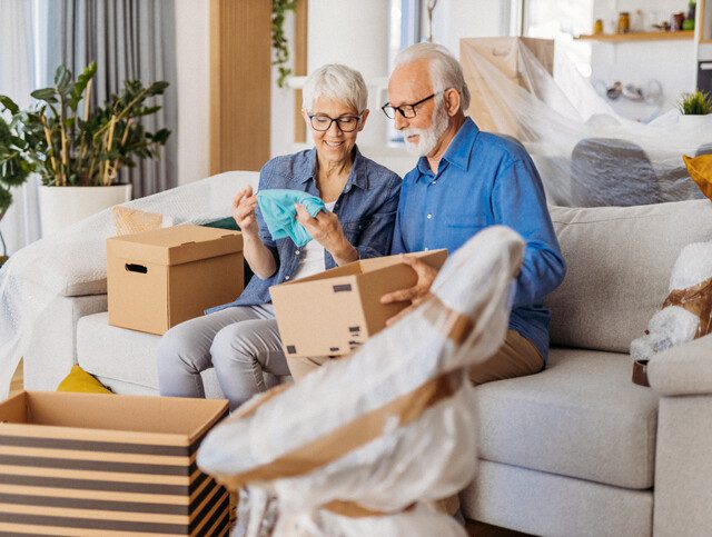 senior couple seated on couch packs their belongings for a move to a senior living community