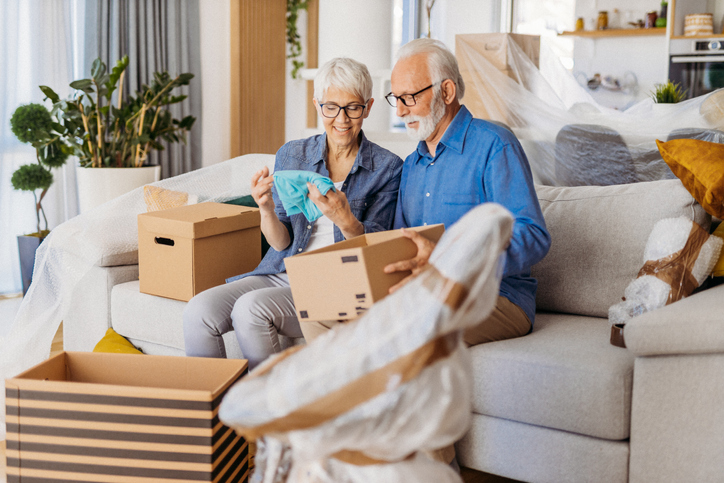 senior couple seated on couch packs their belongings for a move to a senior living community