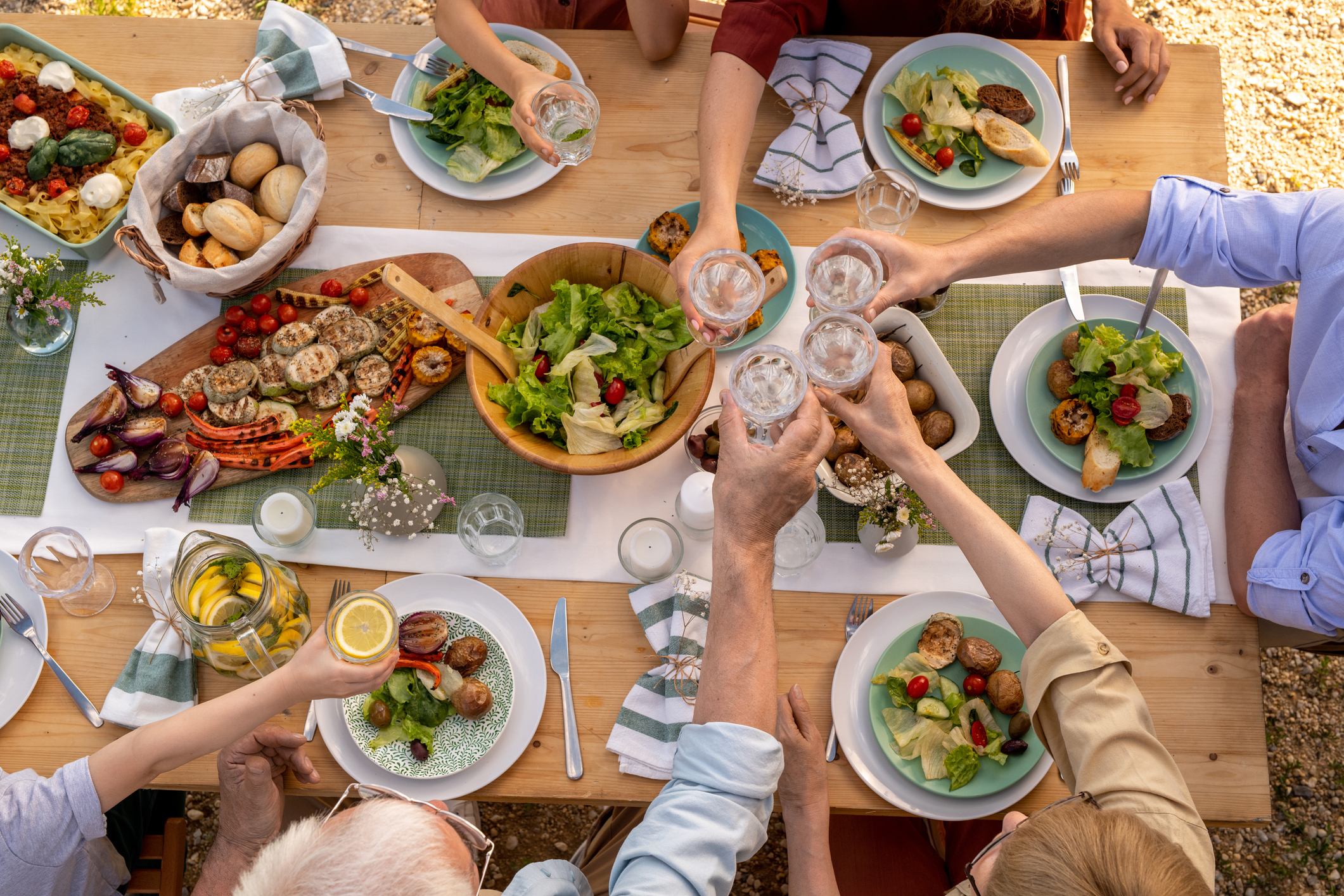 group of seniors toast while enjoying lunch at a picnic table outdoors