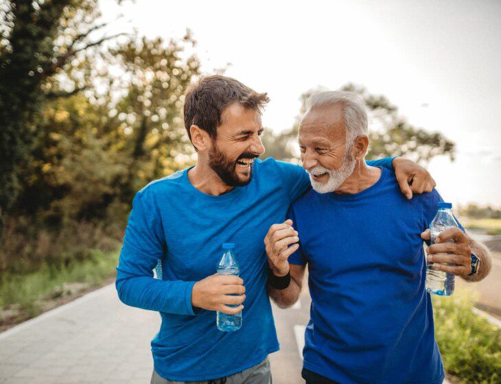 senior man and his adult son laugh together, drinking water after a run