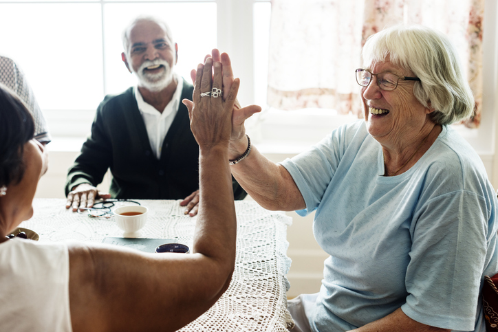 two senior women smile and high-five after winning a board game with friends