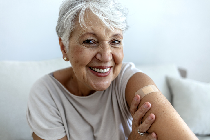 senior woman smiles and shows off her band aid, placed on her arm where she received her vaccine