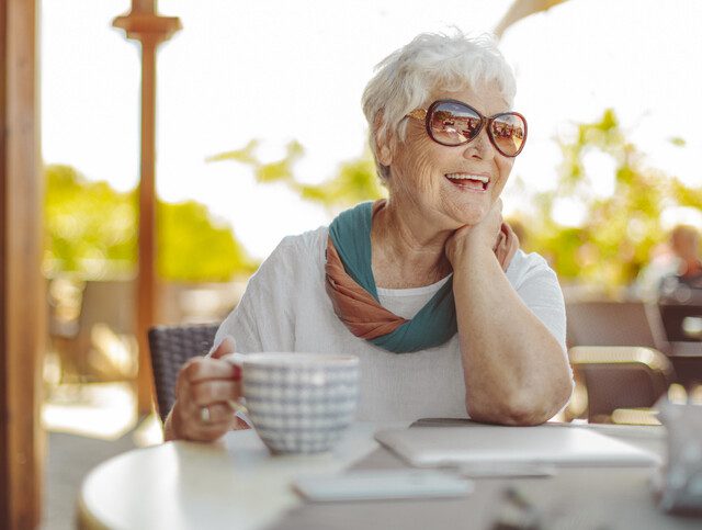 senior woman with fashionable sunglasses holds large coffee cup while seated outdoors, smiling at her companion