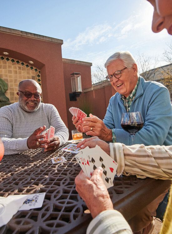 group of seniors play cards and enjoy drinks together in a sunny courtyard terrace