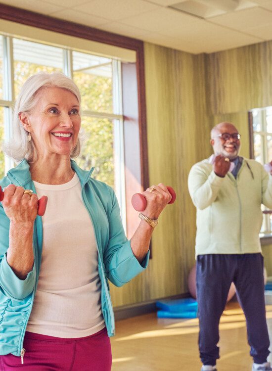 group of seniors smile and lift weights during an aerobics class