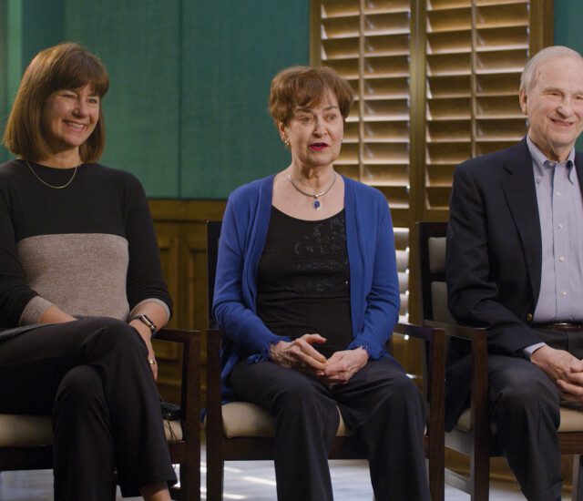 Senior parents and their adult daughter smile and sit in chairs for an interview