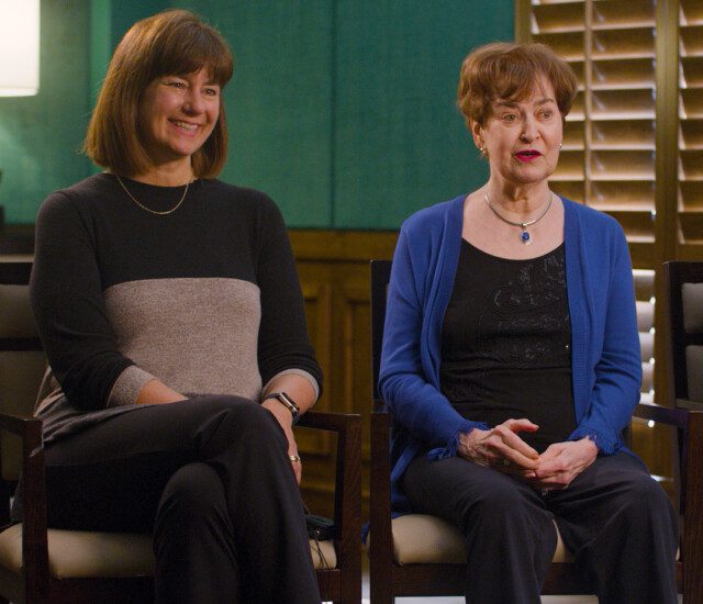 Senior parents and their adult daughter smile and sit in chairs for an interview