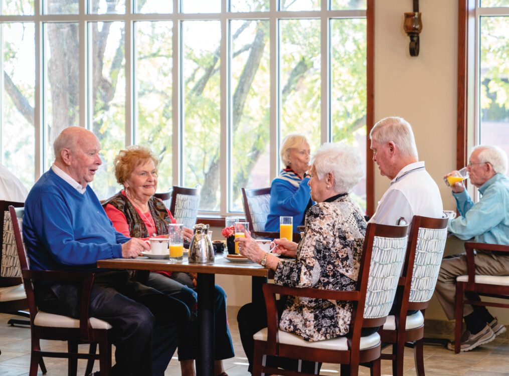 group of seniors sit at a table in a casual dining space for brunch together at Claridge Court Senior Living Community