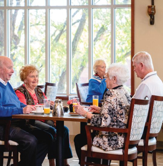 group of seniors sit at a table in a casual dining space for brunch together at Claridge Court Senior Living Community