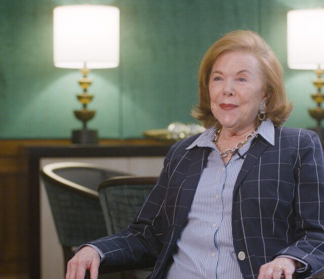 Senior woman in blazer sits in chair for an interview